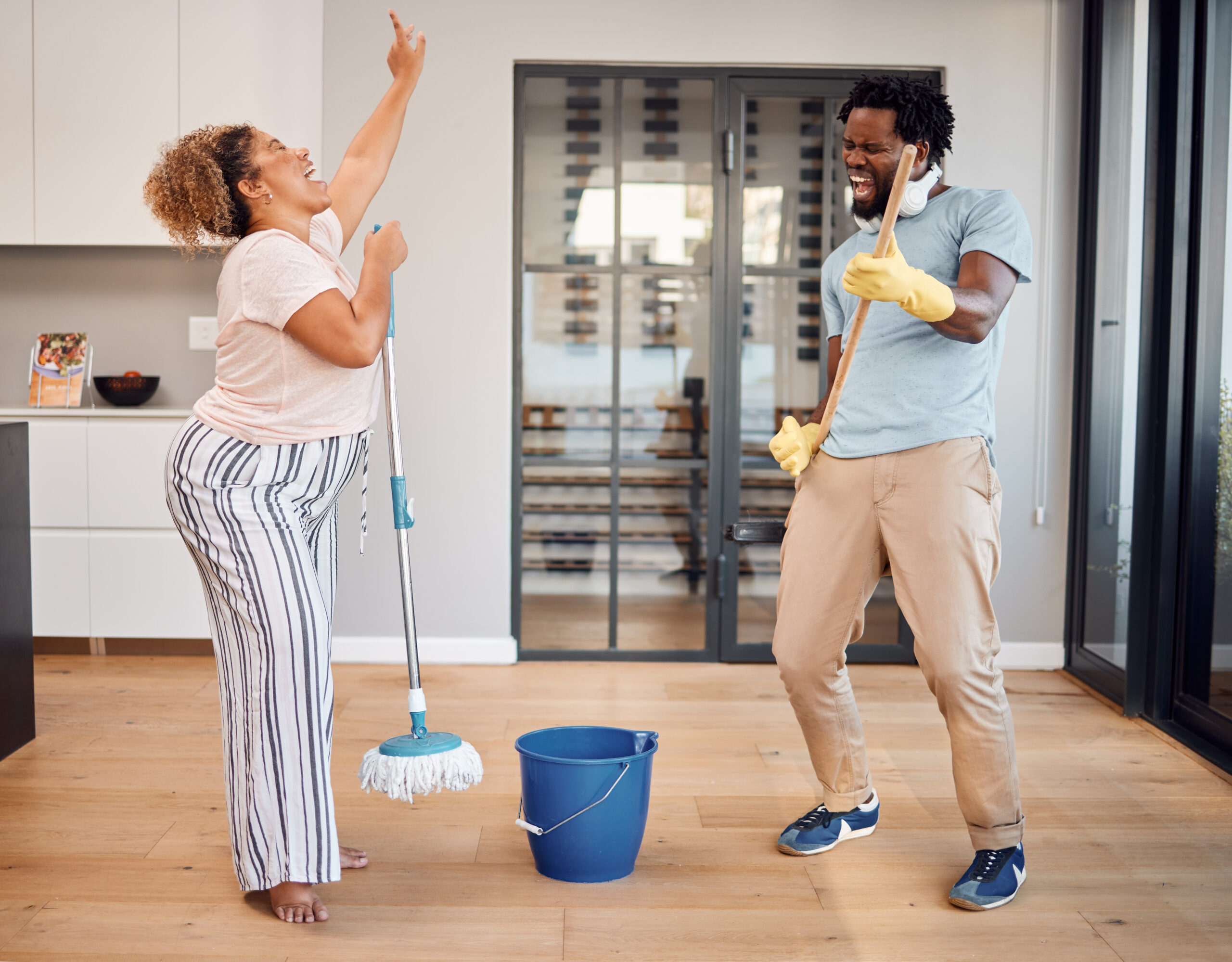 Shot of a young couple singing and dancing while cleaning at home.
